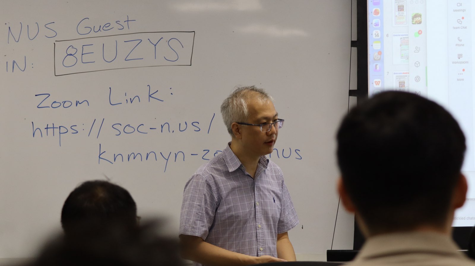 Speaker presenting beside a whiteboard with Zoom details